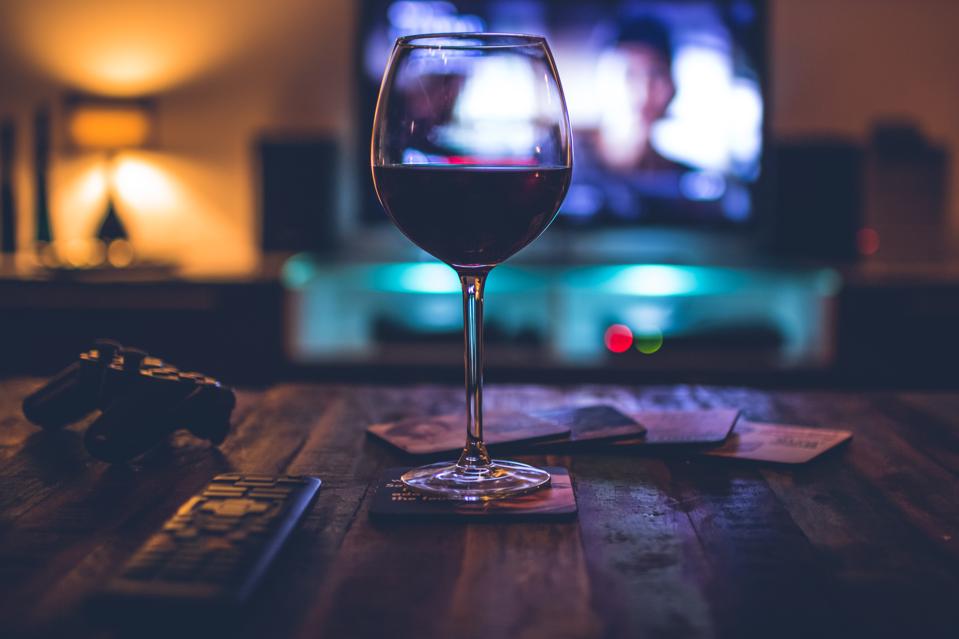 Dark indoor scene with a redwine filled glass in front of a TV