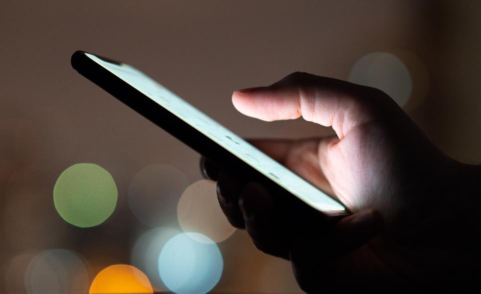 Finger touching smartphone touchscreen at night