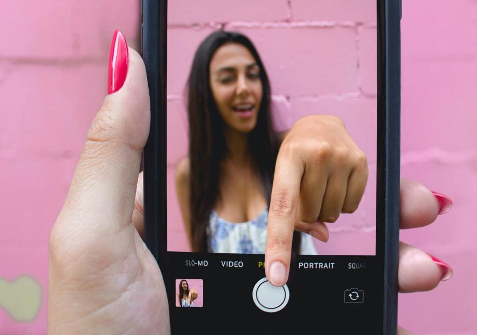 A woman on a smartphone reaching out of the phone to push the camera button