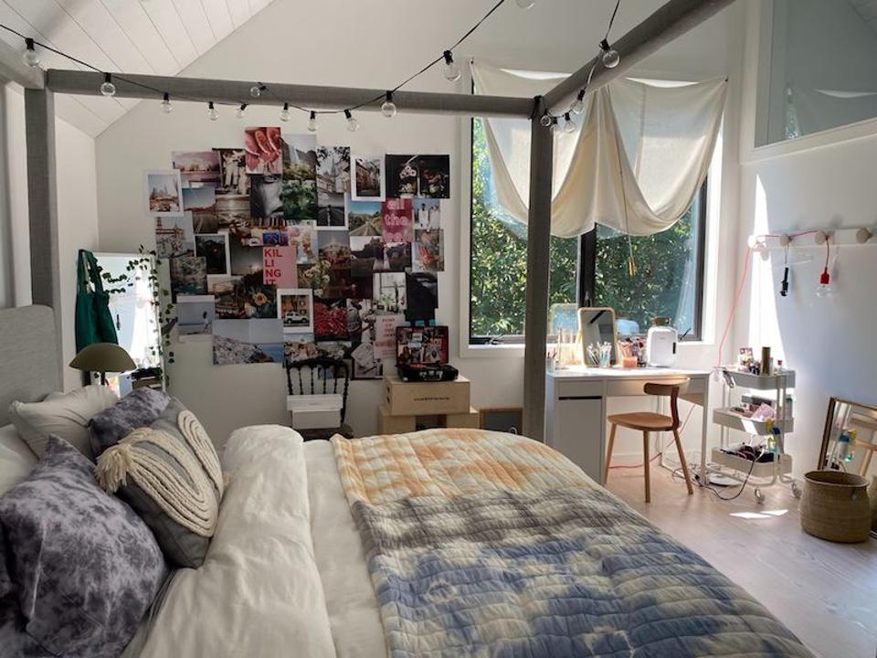 Bedroom with a four poster bed, tie-dye bedding, desk, chair and lots of photos on the wall.