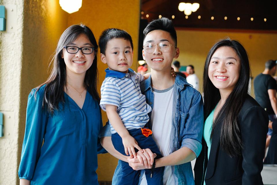 Male Asian student surrounded by family, including two women, and holding a young boy - all smiling for the camera.