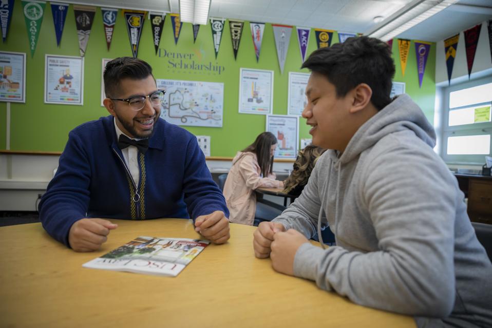 Male advisor with glasses smiling with a male student while discussing a USC Law pamphlet at the Devner Scholarship Foundation center.