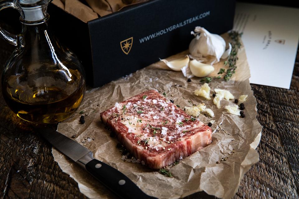 A cut of beef from Holy Grail Steak Co, seasoned with garlic, herbs, and flaky salt.