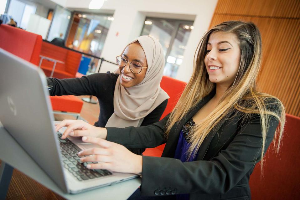two female students sharing a laptop in a school lounge