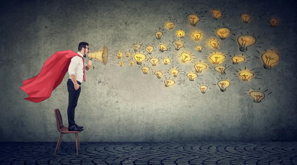 Young super hero businessman standing on a chair screaming in megaphpne spreading new ideas