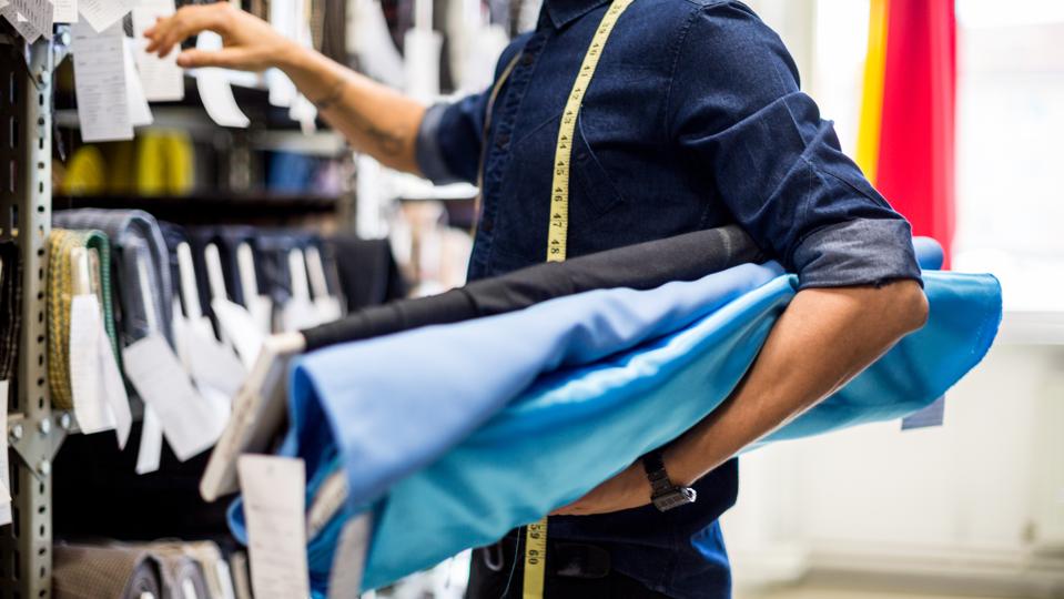 Cropped photo of a male Fashion designer picking out fabric rolls from a display rack.