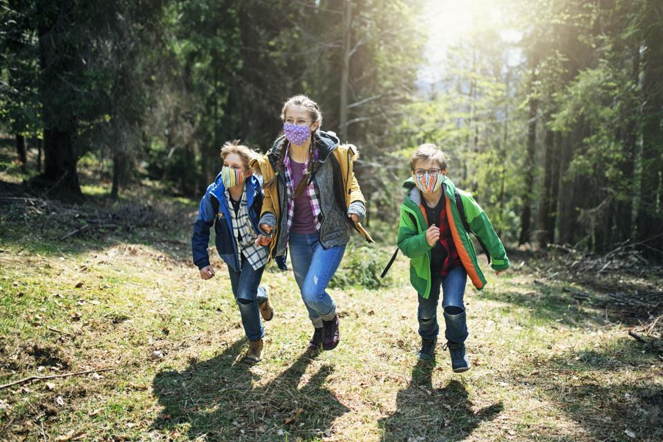 Trois enfants aiment courir dans les bois pendant la pandémie de COVID-19, portant des masques faciaux