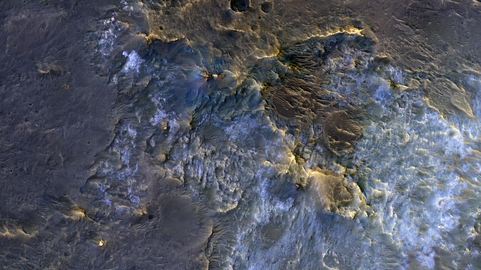 Color photo of a cratered Martian landscape, with rocks showing up in greenish brown and icy blue.