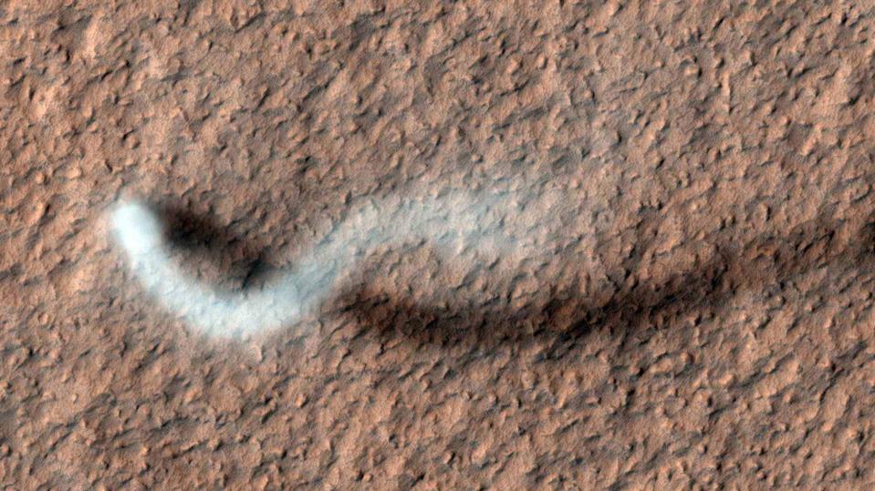 Color photo of a white dust devil moving across a brown landscape, from above.