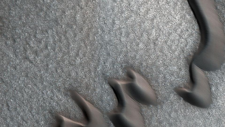 Photo from above of sand dunes moving in rows across an icy surface