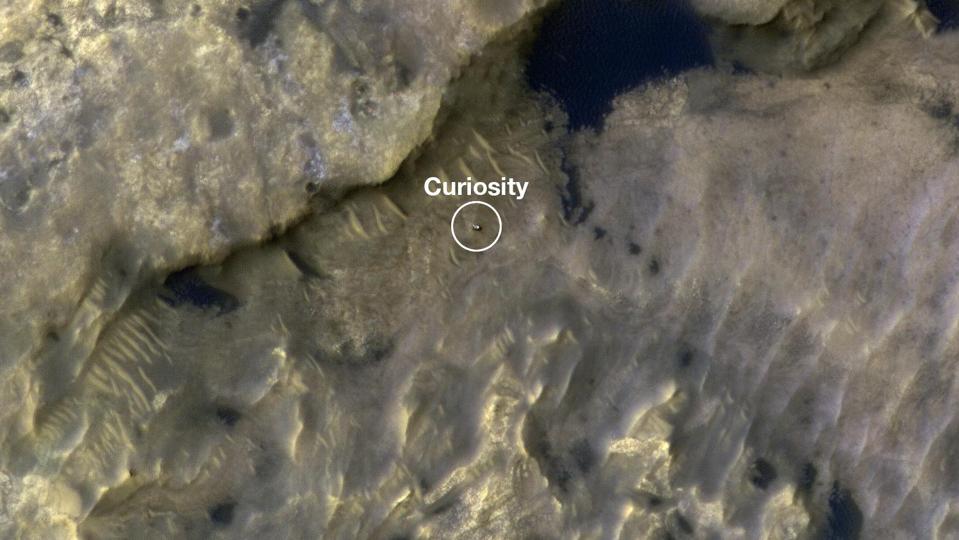 Color photo from above showing a rocky landscape, with a white circle and the word ″Curiosity″ marking the position of a rover.