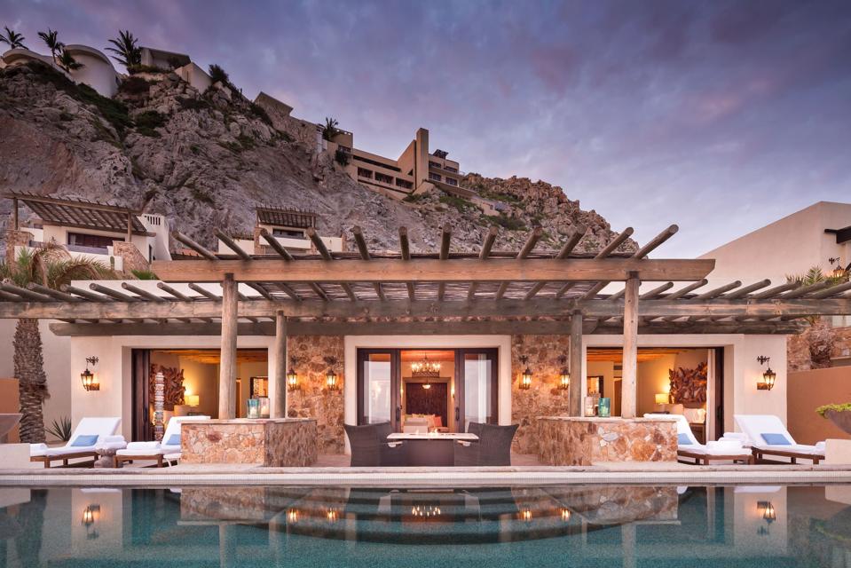 A wood and stone villa with other geometric villas behind it on a hill
