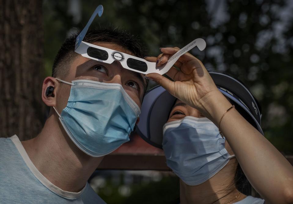 Chinese couple wear protective masks to prevent COVID-19 as they look through protective glasses while watching the sun during the annular solar eclipse outside the Forbidden City on June 20, 2020 in Beijing, China. (Photo by Kevin Frayer/Getty Images)