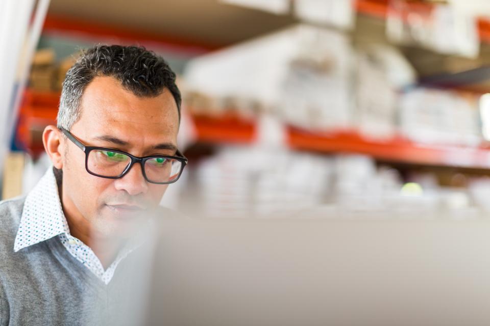 Manager checking stock on a computer in a busy small warehouse