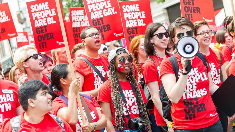 Stonewall volunteers march at London Pride in 2015, with campaign t-shirts, variations on the 'some people are gay get over it' campaign