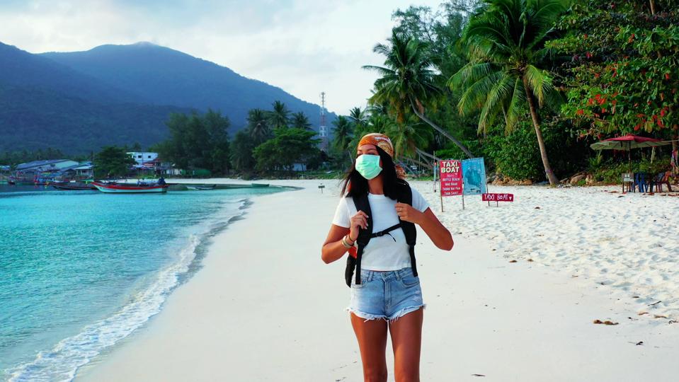 Woman walking alone on empty beach with mask on face protecting from coronavirus.