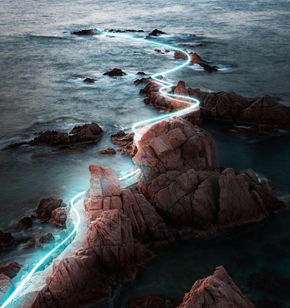 Blue light trail following footpath between the stunning coastline during sunrise.