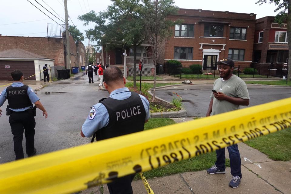 Police secure the scene of a shooting in the Auburn Gresham neighborhood of Chicago and speak with an onlooker on July 21, 2020.