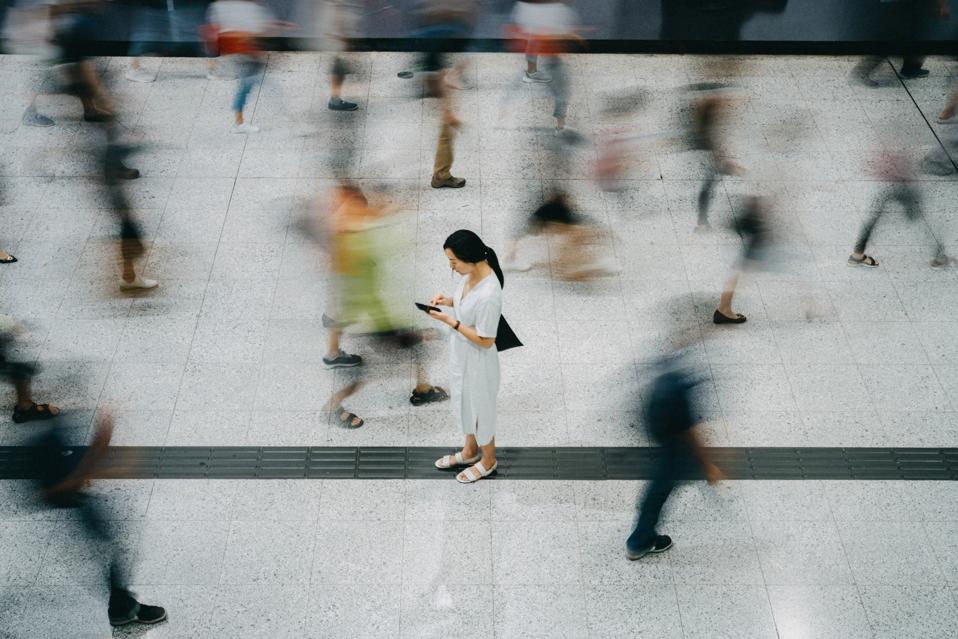 Young Asian woman using smartphone surrounded by commuters rushing by in subway station