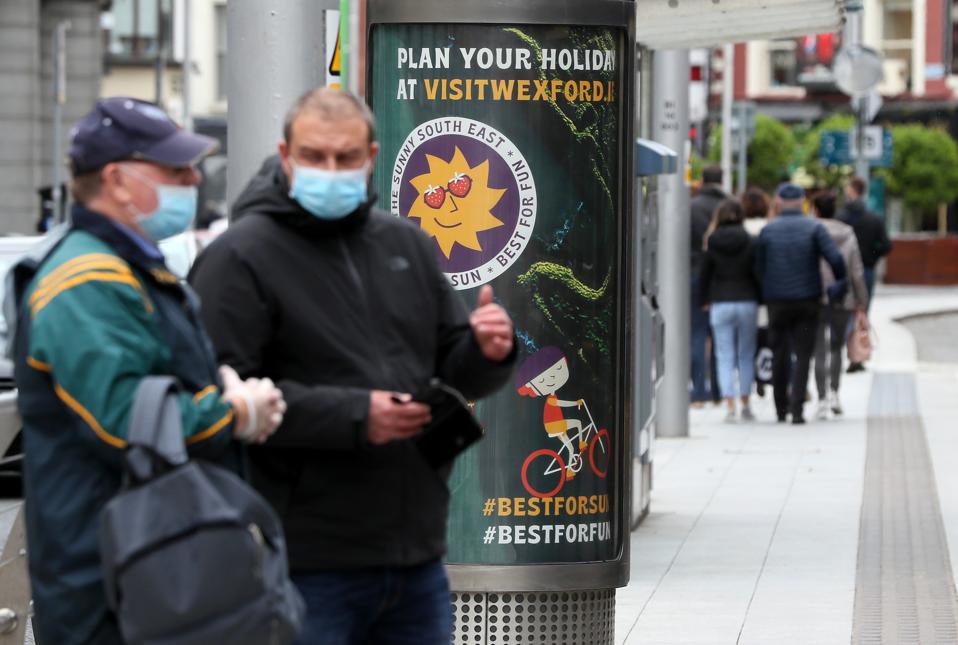 Men in masks by holiday advertisement Ireland no non-essential overseas travel Europe