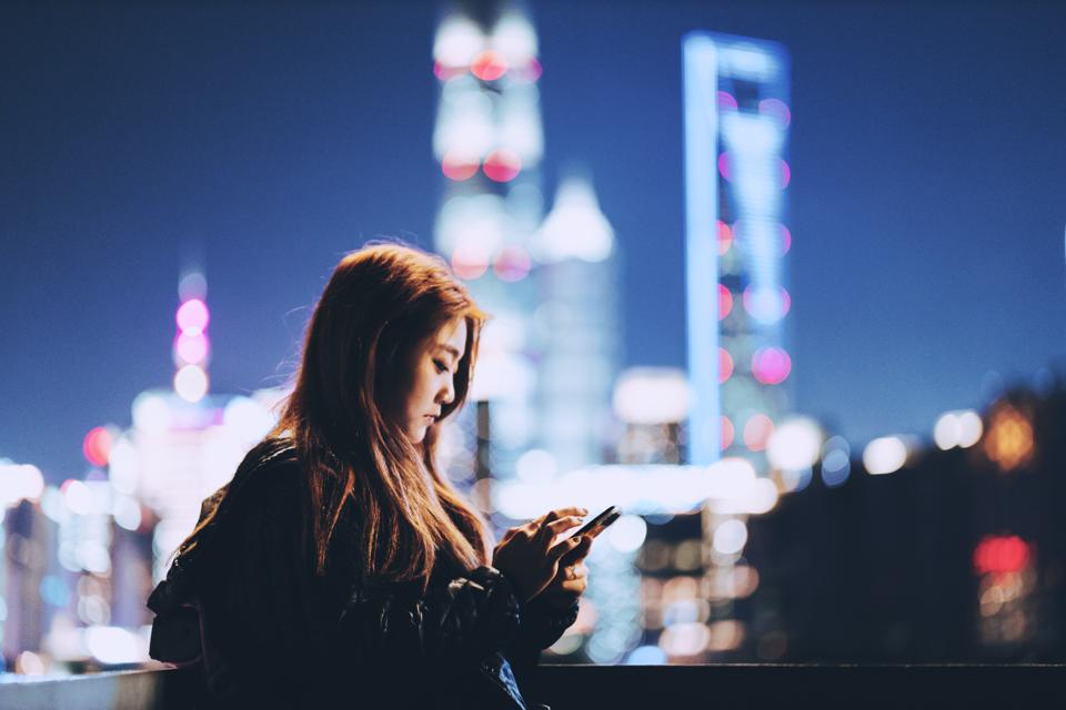 Young woman standing on rooftop using smartphone