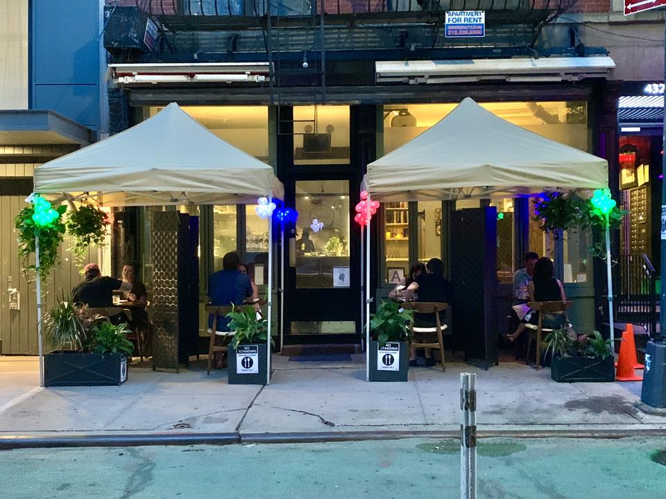 Four tables with a canopy on the sidewalk of a restaurant
