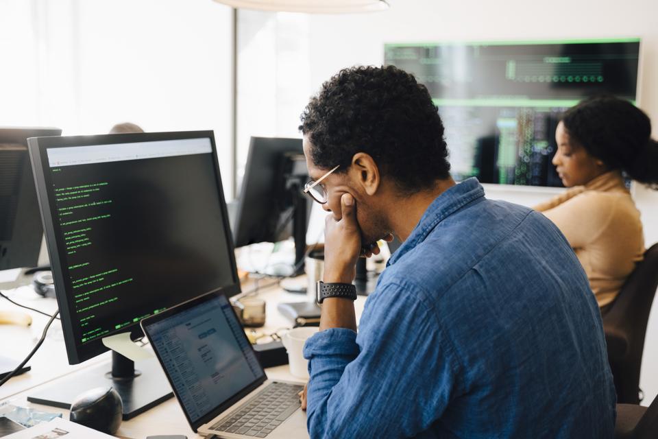Side view of male it professional using laptop while sitting by female coworker in office