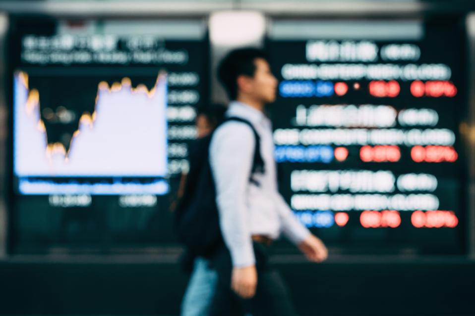 Businessman walking by stock exchange data