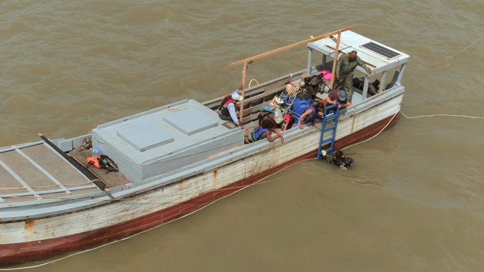 A diver climbs aboard a narrow wooden boat laden with divers and equipment.