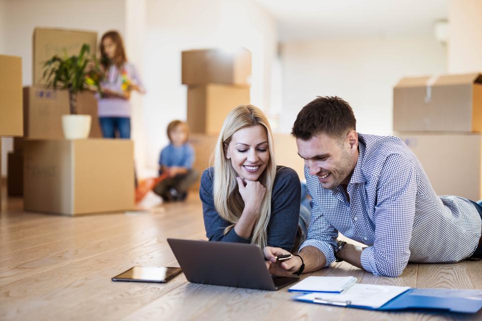 Young happy parents using laptop on the floor at new home.