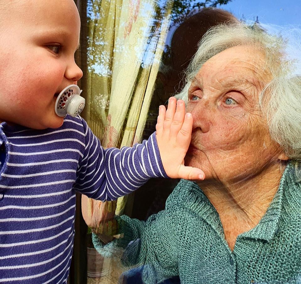 Hold Still: Grandmother and baby kiss through glass window during pandemic