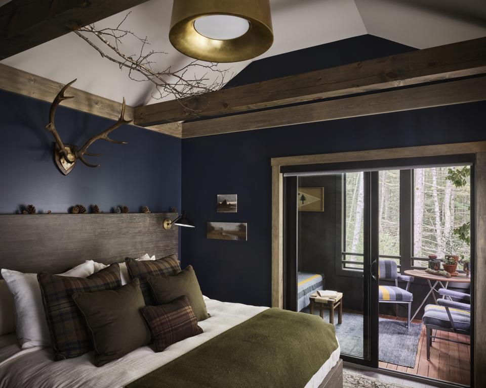 A cozy bedroom with navy walls, wood accents and antlers on the wall.