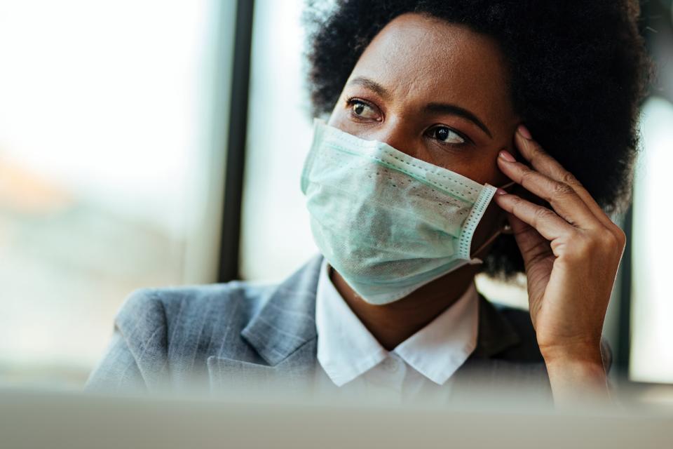 Worried African American businesswoman with protective mask thinking of something in the office.