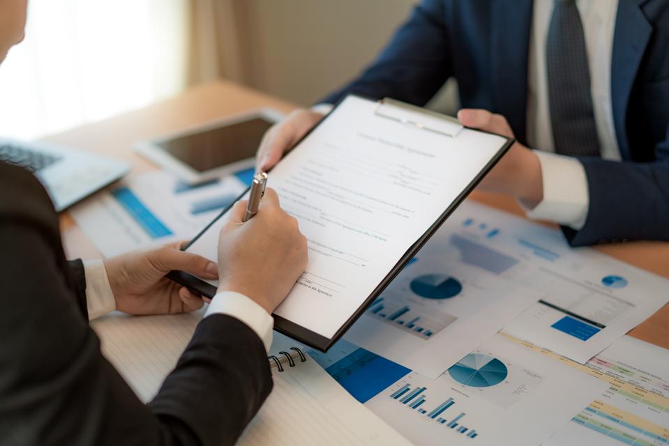 Handsome bearded entrepreneur as his business partner finally signing important contract in office.