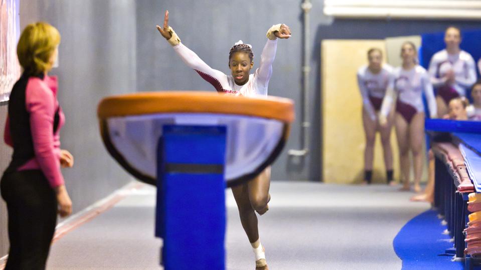 Teammates and Coach Watch Gymnast Performing Vault