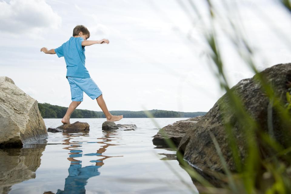 Boy walking barefoot across stones in lake showing small steps lead to career momentum