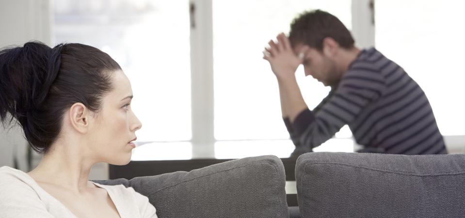 Young woman sitting on sofa, looking at distressed man at table