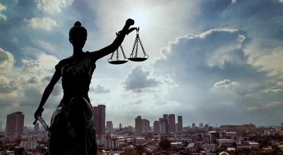 Picture of a female statue with the scales of justice in front of a cityscape