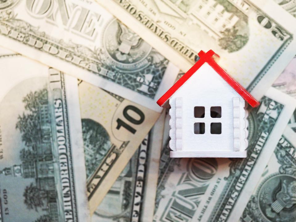Invest in real estate, mortgage concept. White house with a red roof on the background of dollar bills