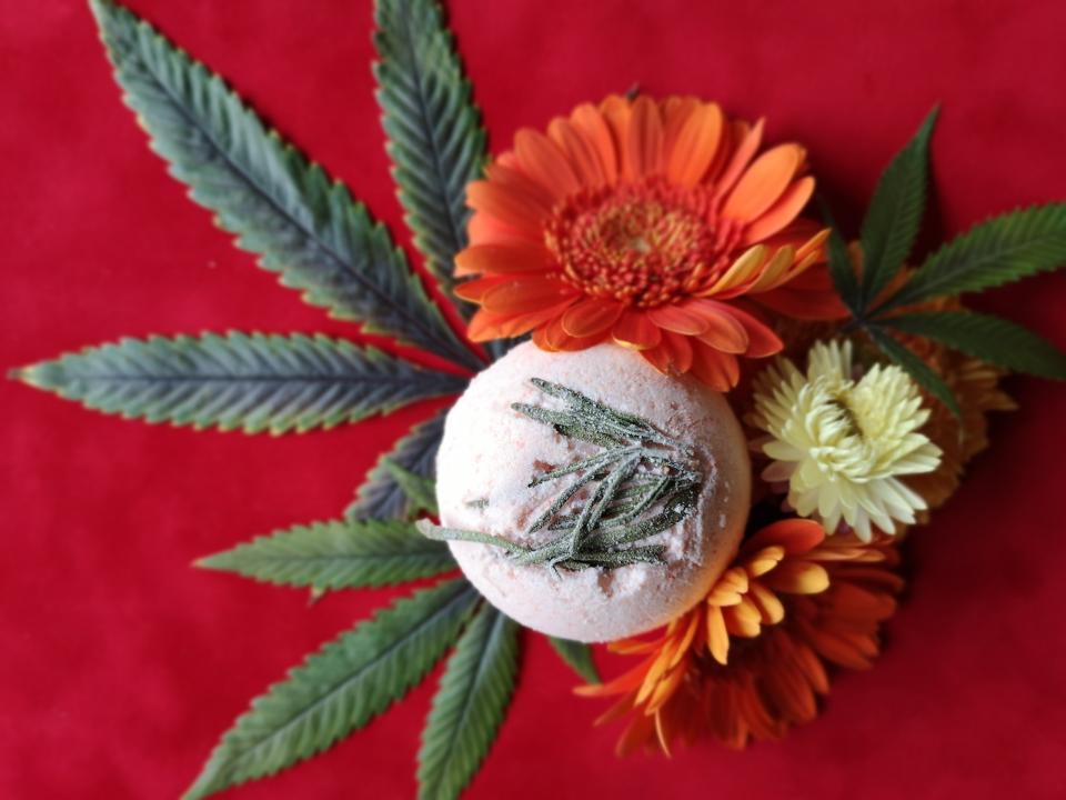 A CBD bath bomb lies on top of a cannabis plant and flowers, made by Arizona-based CBD company Cannabombz.