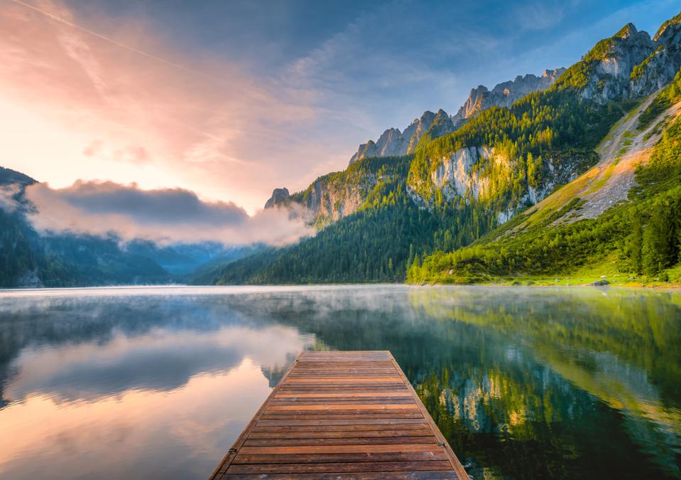 Sunrise Scene of Austrian landscape with forests, fog, meadows, fields and pastures surrounding the lake Gosausee with Alps Mountain
