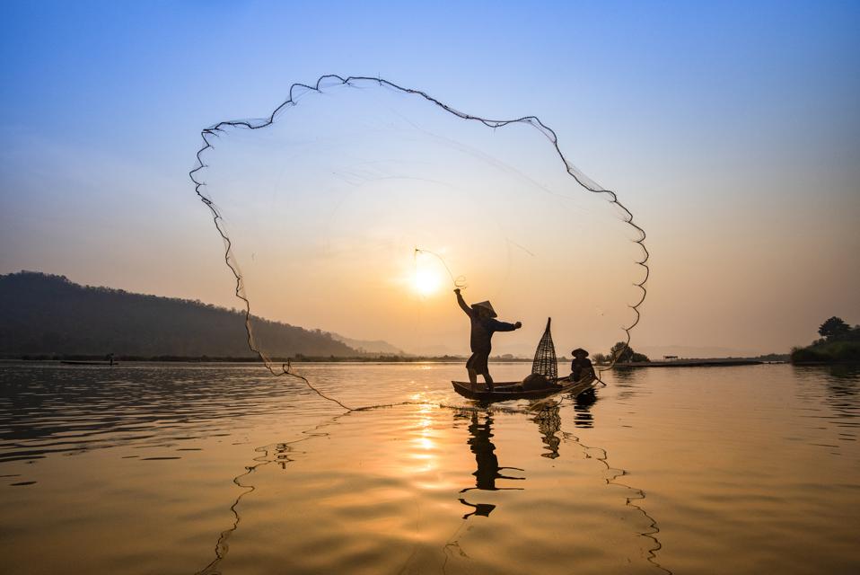 Asia fisherman net using on wooden boat casting net sunset or sunrise in the Mekong river