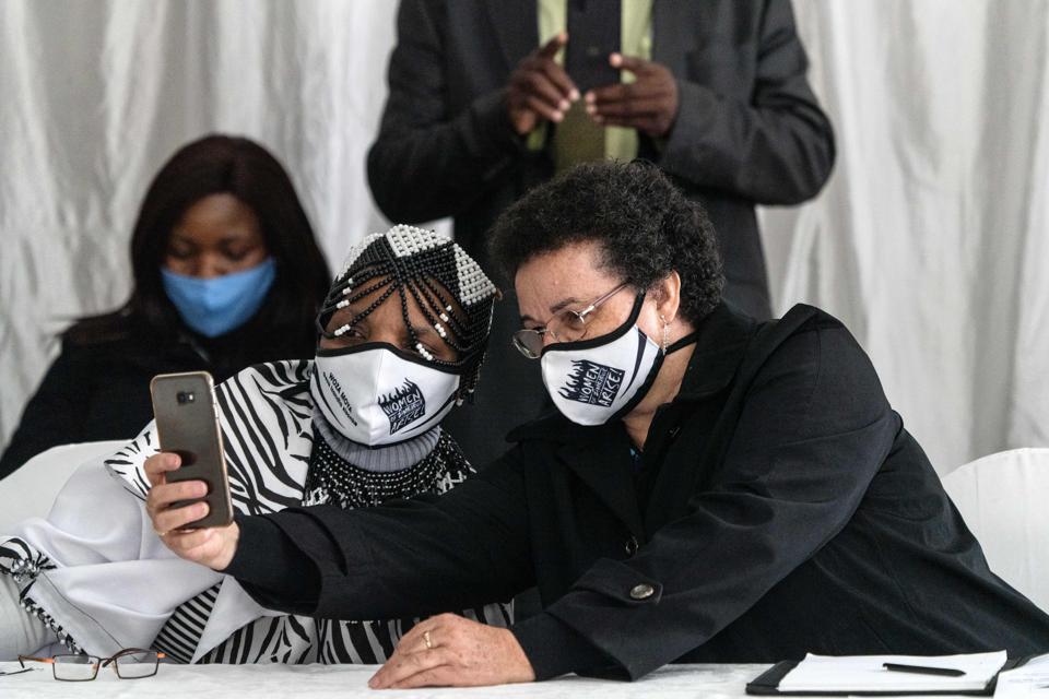 Two women wearing masks take a selfie in a meeting room