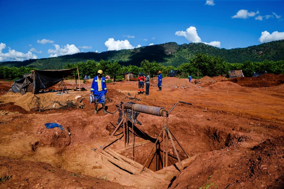 Reddish earth with a square hole carved into it, and men in hats