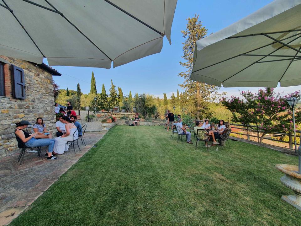 wine tasters sit at tables on the lawns of Chianti Classico winery Il Palagio in Panzano