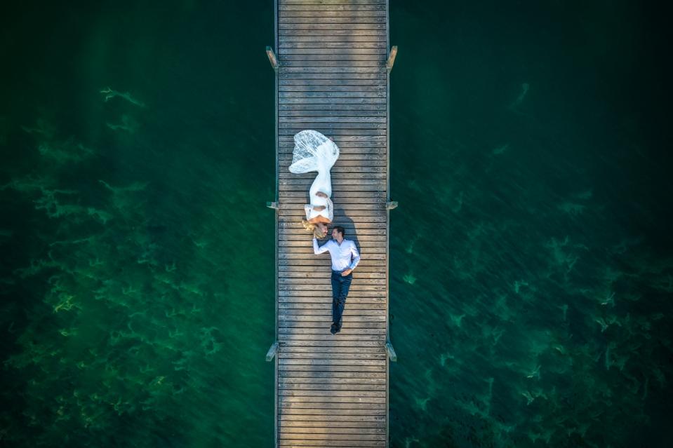 Photo de mariage gagnant du prix de Sienne d'un couple allongé sur un long quai prise avec un drone