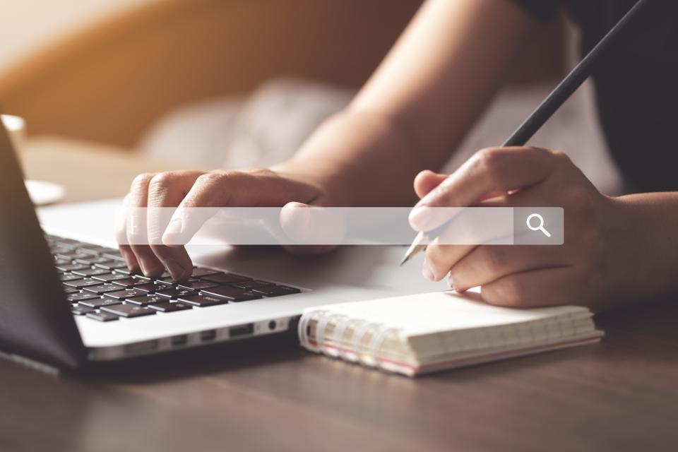 Cropped Hands Of Woman Writing In Diary While Using Laptop On Table
