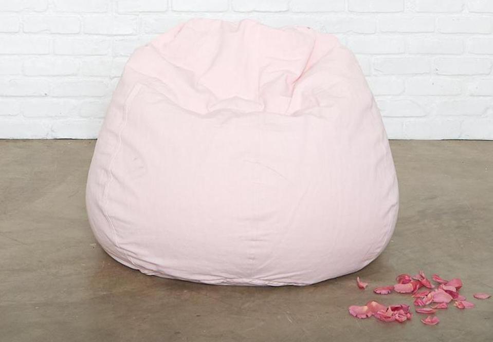 A pink beanbag chair on a concrete floor with a brick wall and petals