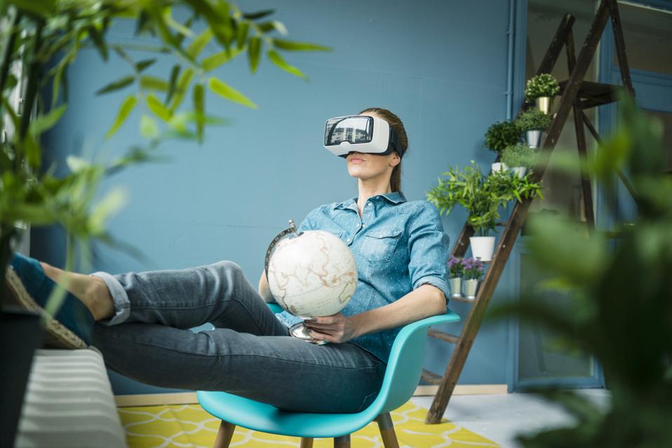 Beautiful woman sitting in her home, decorated with plants, holding globe, wearing VR glasses