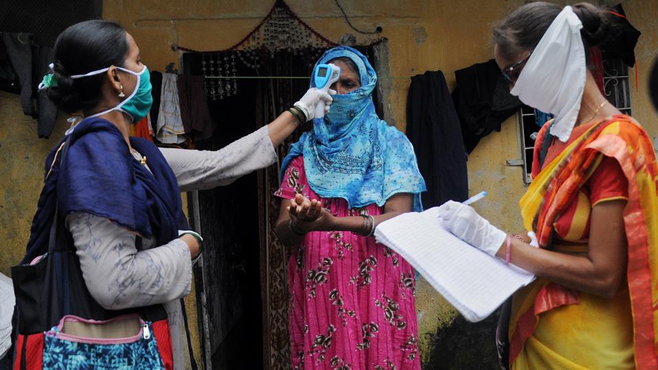 Community healthcare volunteer checks temperature of a woman...